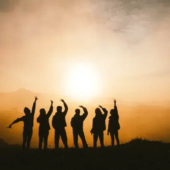 un groupe de personnes en haut d'une montagne au coucher du soleil qui lève les mains